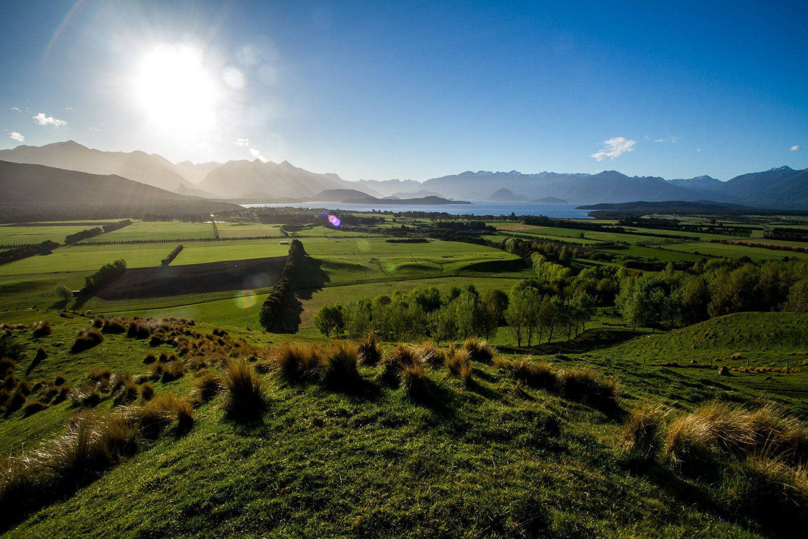 Una vista panorámica de un paisaje verde y exuberante con colinas onduladas y montañas distantes bajo un cielo despejado.