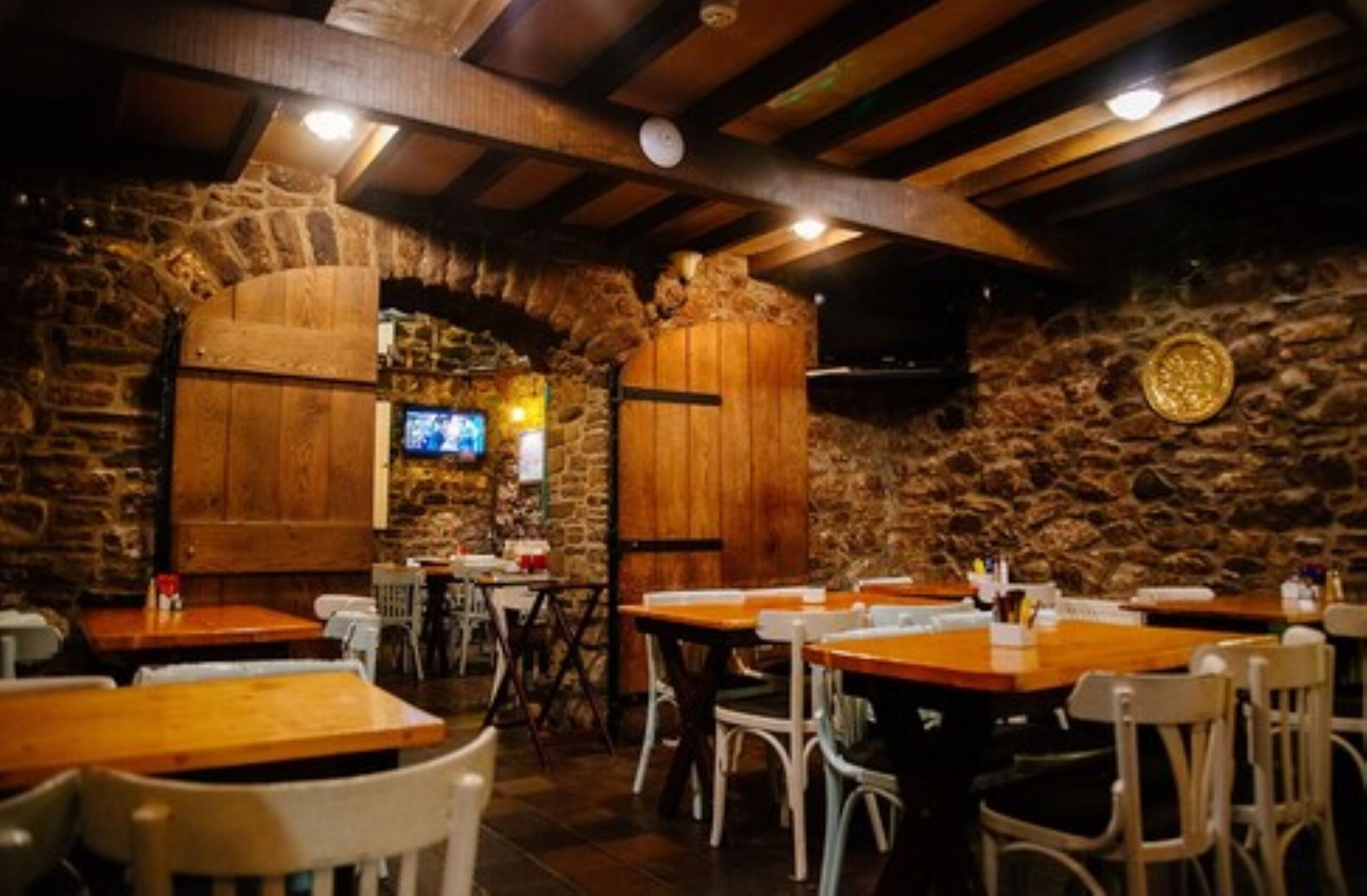 A restaurant with stone walls, wooden tables, and white chairs.