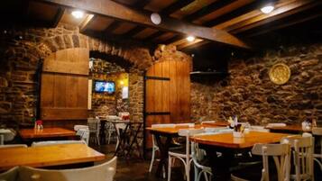 A restaurant with stone walls, wooden tables, and white chairs.