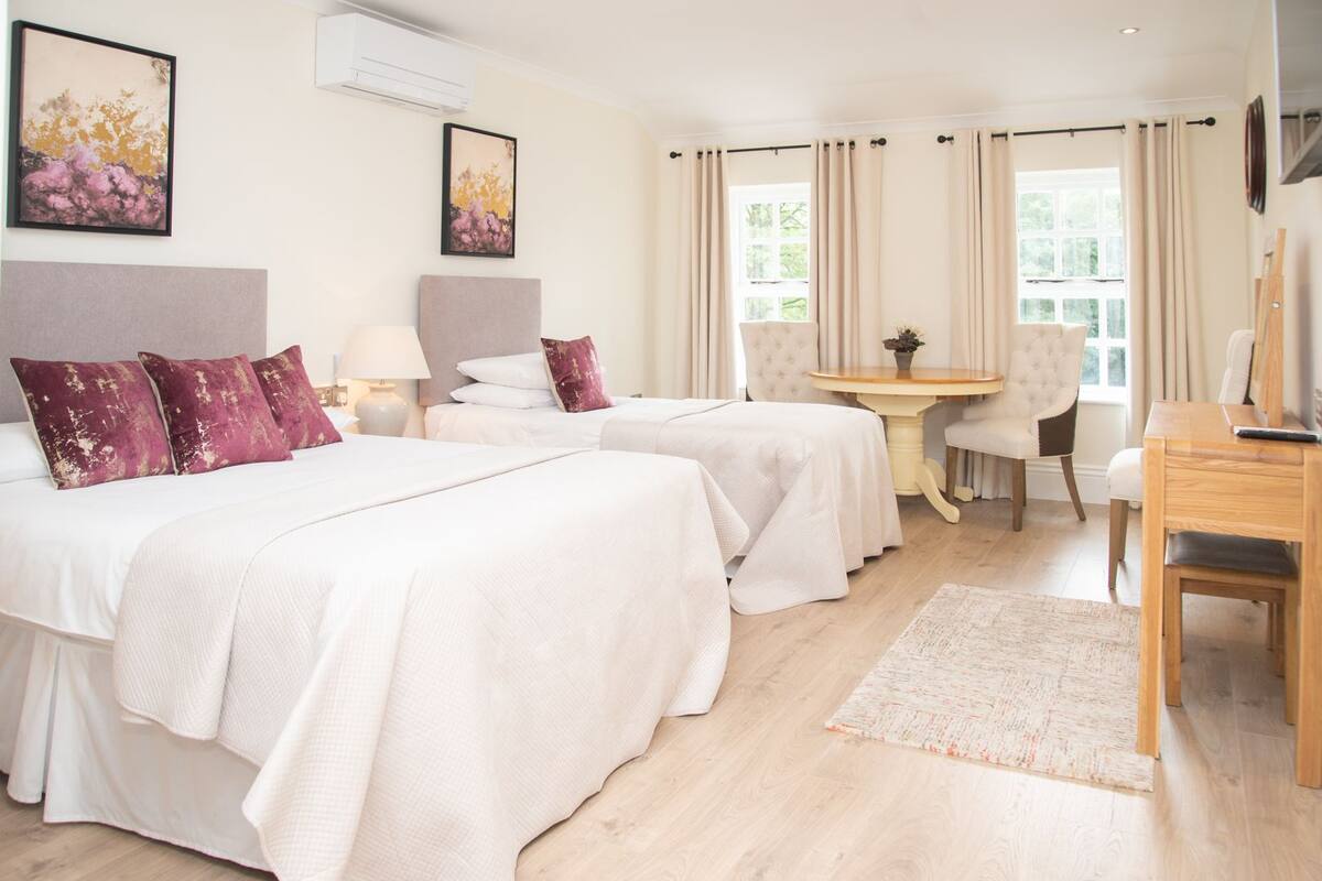 A hotel room with two beds, a small table, a chair, and a desk.