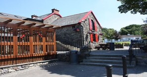 A stone building with red shutters and a wooden pergola.