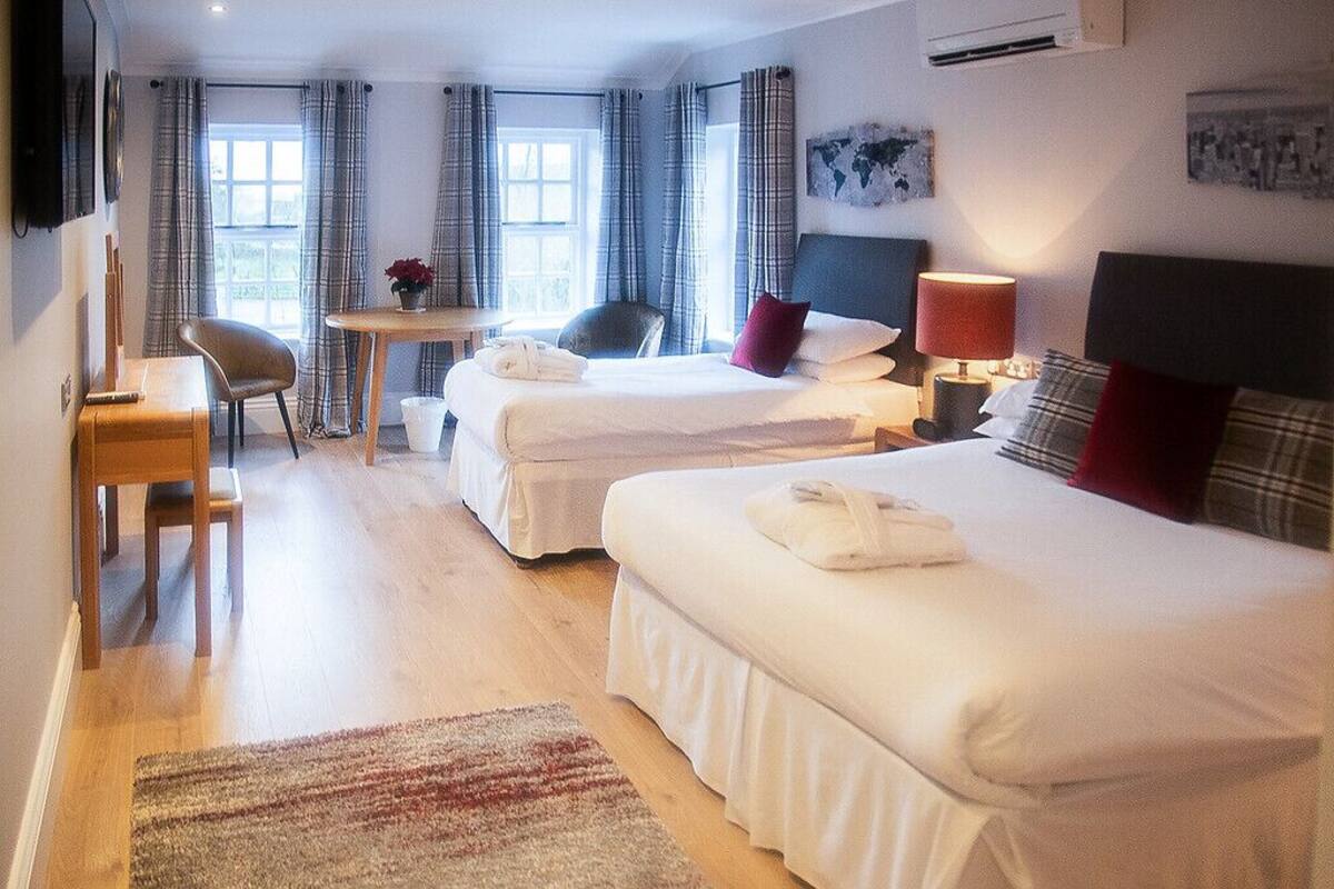 A hotel room with two beds, a desk, a chair, and a small table.