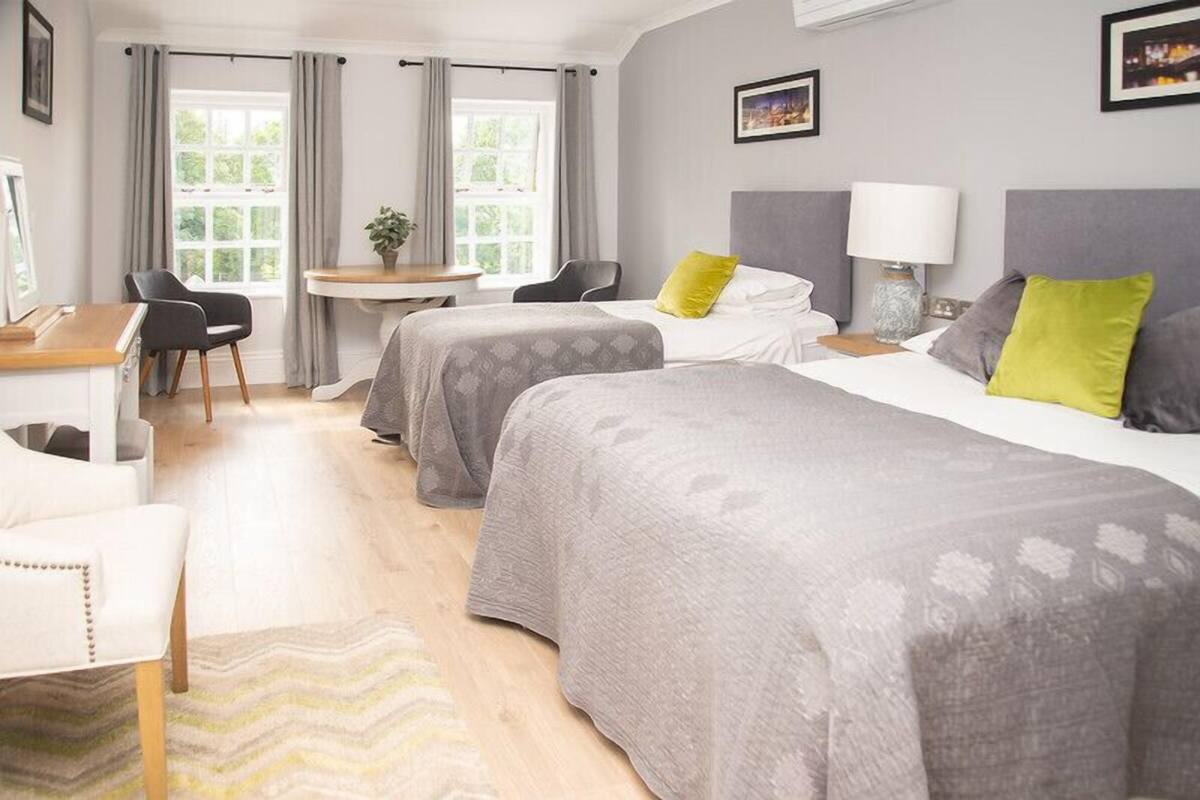 A hotel room with two beds, a desk, a chair, and a window with curtains.