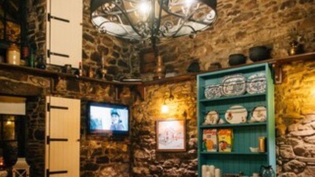 Interior rústico de restaurante con paredes de piedra, mesas de madera y un televisor montado en la pared.