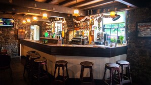 Un bar con pared de piedra, mostrador de madera, taburetes y luces colgantes.