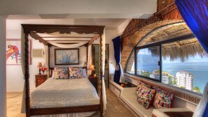 Une chambre à coucher avec un lit à baldaquin, une fenêtre donnant sur la mer et un balcon doté d’un toit de chaume.