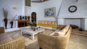 Un salon comprenant un canapé, deux fauteuils en osier, une table basse, une cheminée et une horloge murale.