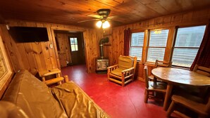 A cabin interior with a wooden floor, a sofa, a rocking chair, a table, and a fireplace.