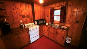 A compact kitchen with wooden walls, a white stove, a microwave, and a sink.