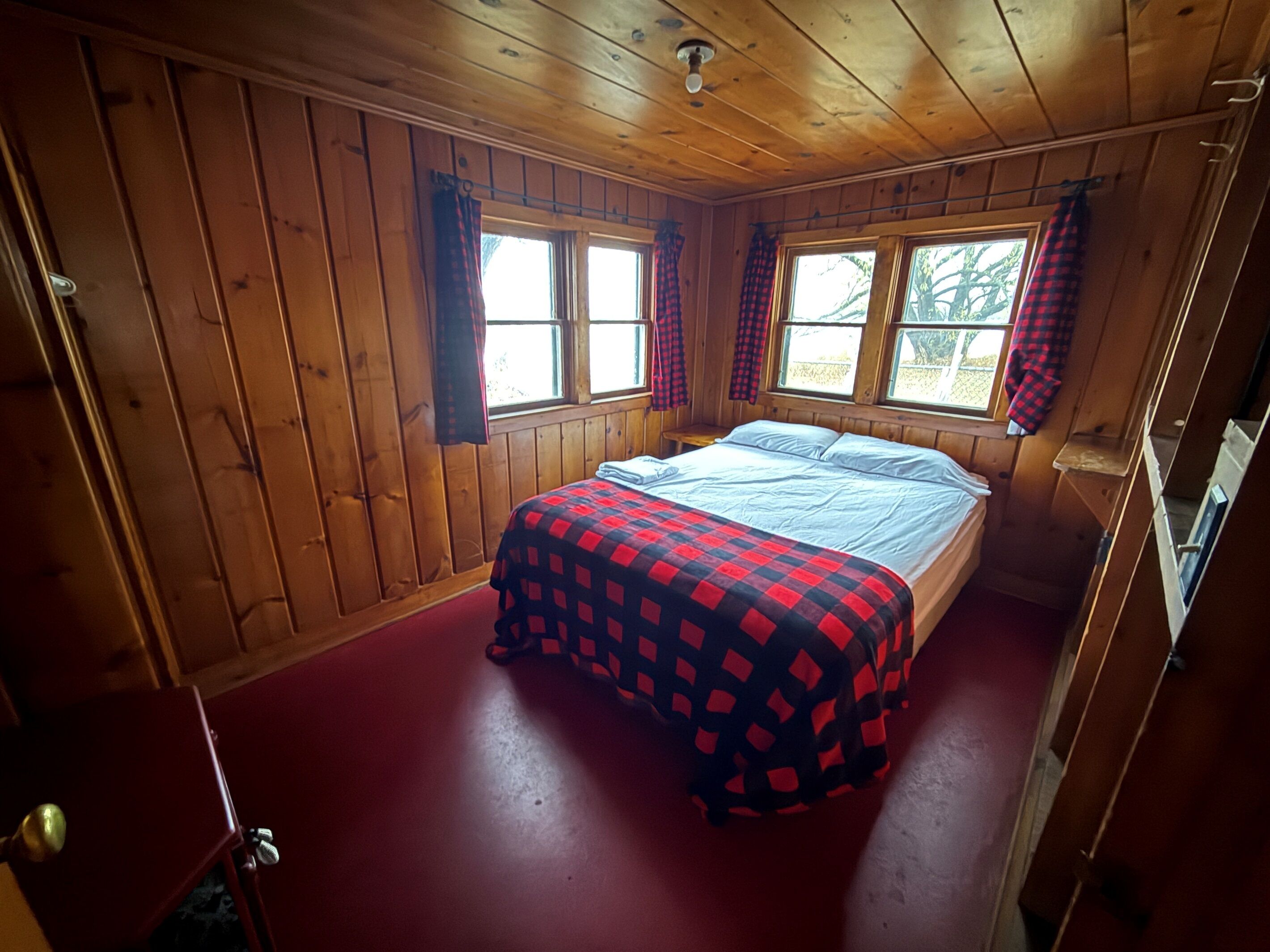 A wooden cabin bedroom with a bed, windows, and curtains.