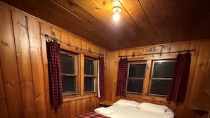 A wooden-paneled room with a bed, two windows with curtains, and a red carpet.