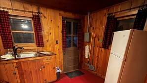 A compact kitchen with wooden walls, a red floor, a sink, a stove, and a refrigerator.