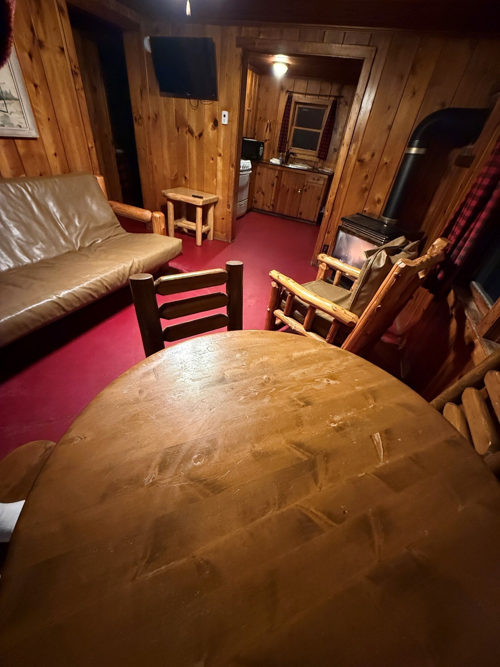 A cozy cabin interior with a wooden dining table, a sofa, and a kitchen area.