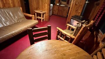 A cozy cabin interior with a wooden dining table, a sofa, and a kitchen area.