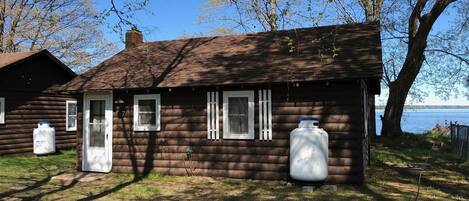 A log cabin with two large water tanks, a door, and windows.