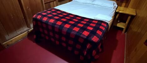 Una habitación de madera con una cama, un ventanal y un suelo rojo.