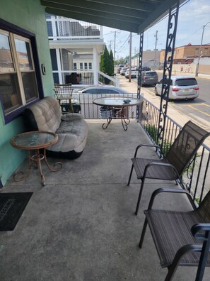 A covered porch with a sofa, two tables, and chairs.