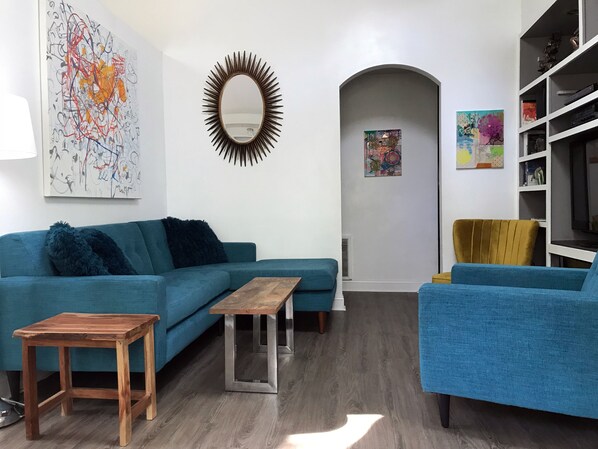 Relax in this stylish living room with a teal sofa, wooden coffee table, and unique sunburst mirror.
