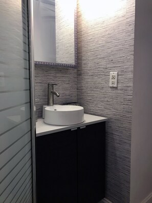 Modern bathroom with a sleek sink, gray tile walls, and a cabinet for storage.