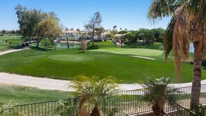 Un campo de golf con un obstáculo acuático, palmeras y un cielo azul despejado.