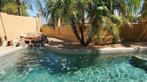 Una piscina cristalina con una pequeña cascada rodeada de rocas y palmeras.