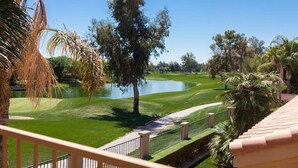 Campo de golf con un obstáculo acuático, palmeras y un cielo azul despejado.