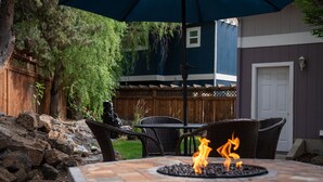 An outdoor patio with a stone table, a fire pit, wicker chairs, and a blue umbrella. - Great location in Old Mill District ! ♥ Fenced Backyard,  ♥ Pet Friendly! (Bend)