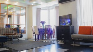 A modern living room with a sofa, a TV, a dining table with chairs, and a large window with curtains. - Tbilisi Center Private 4-room Apartment (Dzveli Tbilisi)