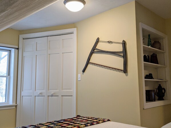 A room with a white door, a shelf with kitchen items, and a colorful blanket on the bed.