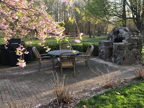 Relax in a serene garden setting with a round table, wicker chairs, and a stone fireplace.