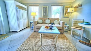 A living room with a beige sofa, a coffee table with a tray of food, a lamp, and a sign that says "BEACH" on the wall. - Cottage Priv. Pool & Tennis Beach 5 min Central (Paget)