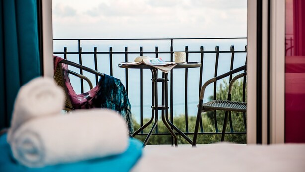 A balcony with a metal railing, a small table with a book and a mug, and a chair. - Lourdas bay great view - Studio Maria (Kefalonia)