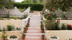 A staircase with white steps leading up to a stone wall, surrounded by various potted plants and flowers. - Lourdas bay great view - Studio Maria (Kefalonia)