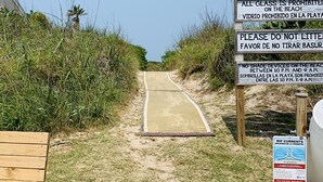Uma trilha de praia com placas indicativas e um banco de madeira.