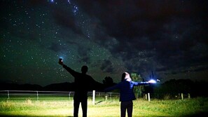 Zwei Personen beobachten den Sternenhimmel vor einem sternübersäten Hintergrund.
