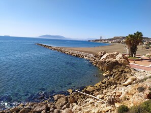 Vista costeira com mar azul límpido, linha costeira rochosa e uma cordilheira distante.