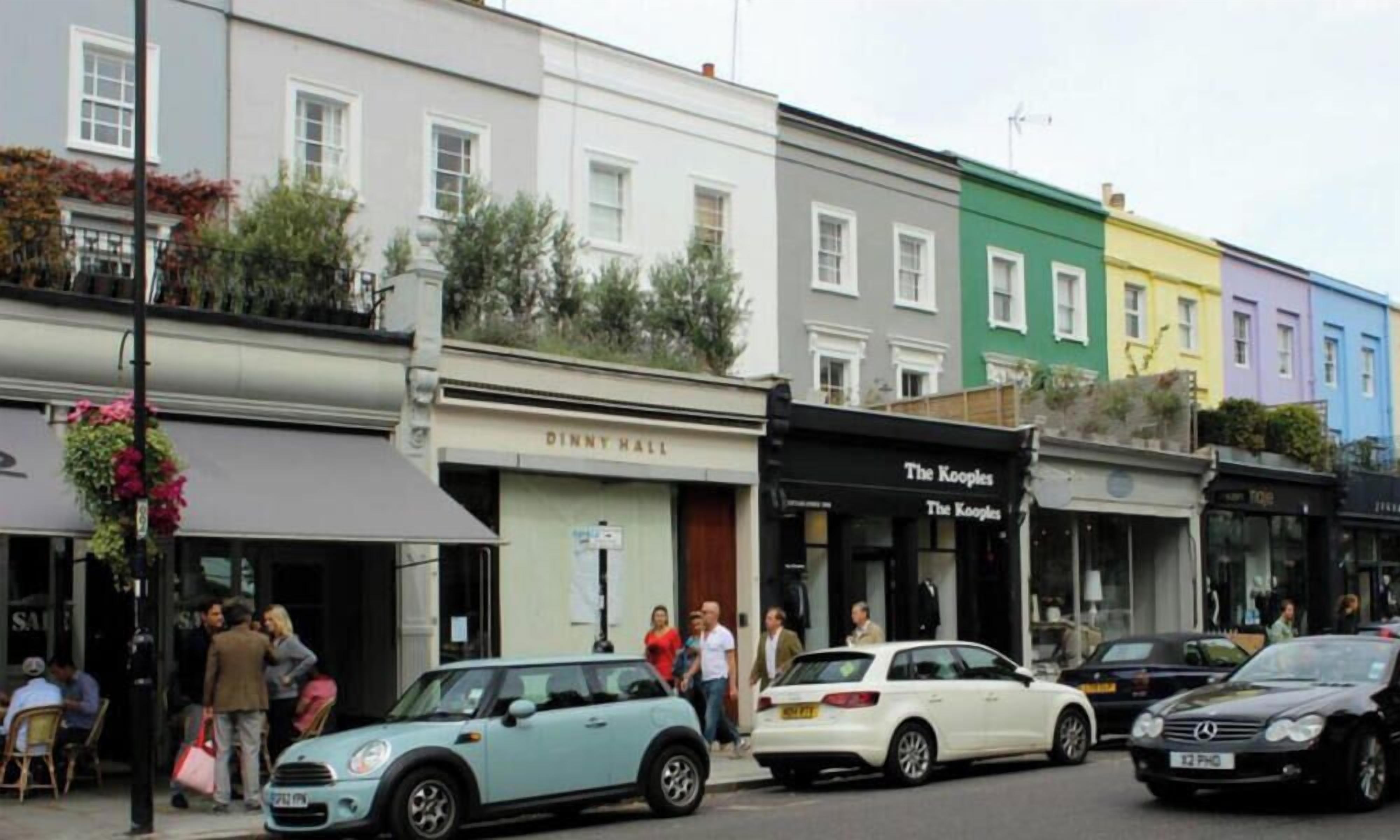 A street with colorful row houses, a shop named 'The Kooples', and parked cars.