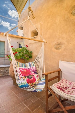 A hammock chair with a colorful cushion, a wooden chair, and a potted plant with red flowers.