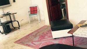 A living room with a sofa, a television, a small table, and a chair. - A large quiet blue flag apartment with free wifi modern and well equipped (Sousse)