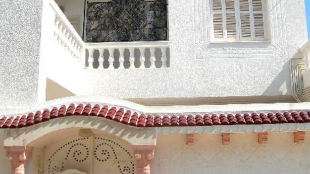 A white building with a balcony, a window with shutters, and a decorative door with a patterned design. - A large quiet blue flag apartment with free wifi modern and well equipped (Sousse)