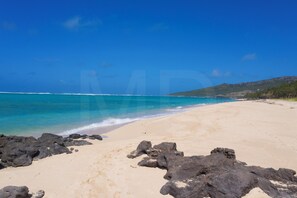 A beach with clear blue water, sandy shore, and rocky outcrops.