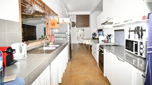 Cocina compacta con horno integrado, microondas y lavabo. Cuenta con una zona de comedor con una mesa y sillas blancas.