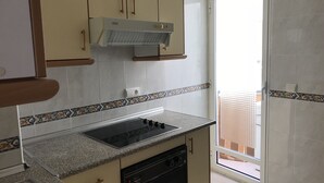 Une cuisine équipée d’une cuisinière intégrée, d’un lave-vaisselle et d’une fenêtre donnant sur un balcon.