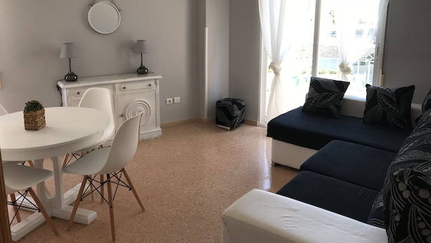 Un espace de vie compact comprenant une table à manger, des chaises, un canapé, un petit meuble et une fenêtre agrémentée de rideaux légers.