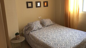 Une chambre à coucher avec une couvre-lit à motifs, une petite table ronde ornée d’un pot de fleurs et deux miroirs fixés au mur.