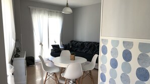 Un espace repas comprenant une table ronde, des chaises blanches, un canapé et un mur décoré de motifs.