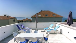 A rooftop terrace with a table and chairs, a view of the sea, and a building with a tiled roof. - Apartment with a Terrace and Free Parking - Beach Nearby (Split)