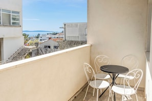 Un balcón con mesa y sillas, vista al mar y un edificio al fondo.