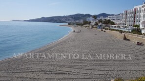 A beach with a stone walkway, a hotel building, and a mountain in the background. - Live the Charm of Nerja – Steps from the Beach and Historic Center (Nerja)