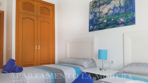 Une chambre d’hôtel avec deux lits, une armoire en bois, un tableau représentant des nénuphars et une lampe.